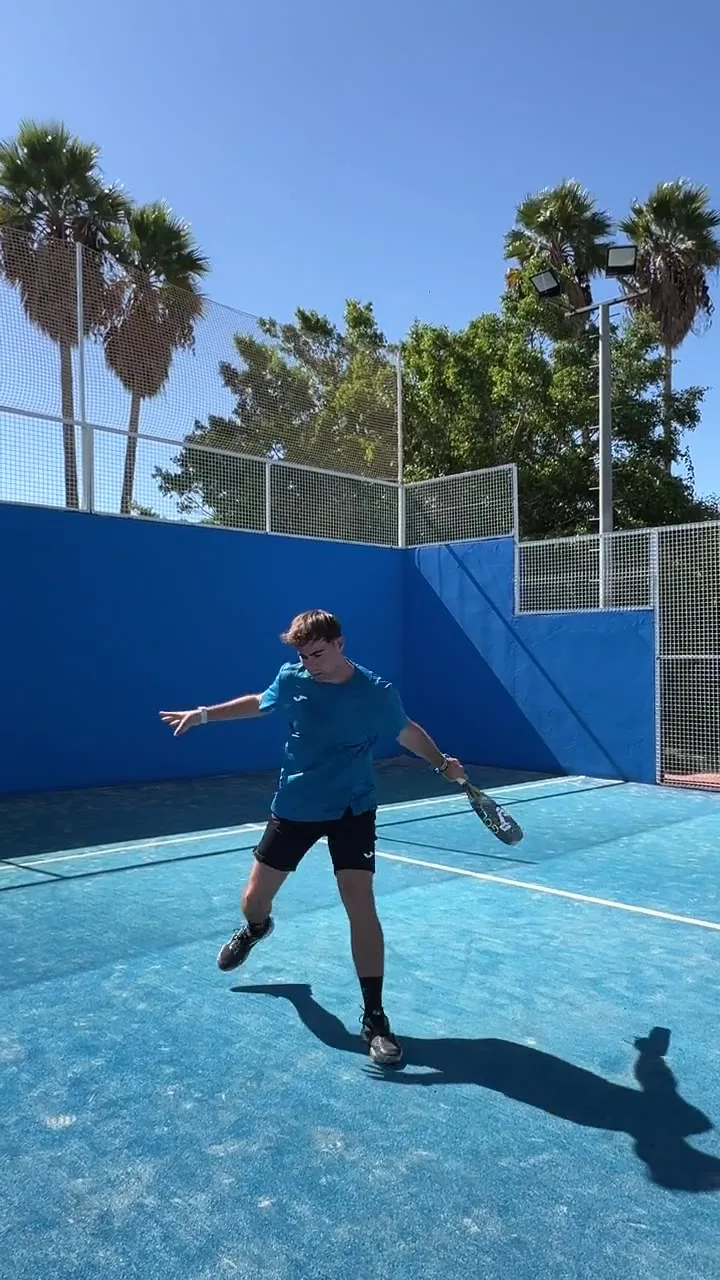 Padel school coach hitting on a club court, palm trees behind