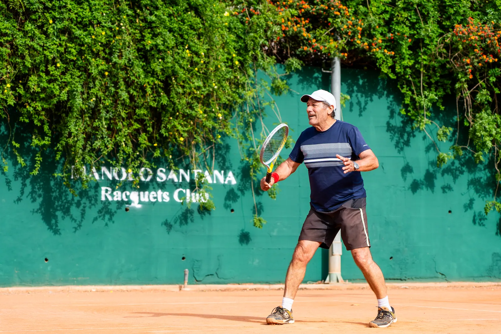 Alumno adulto jugando en pista de tierra batida junto al muro del club