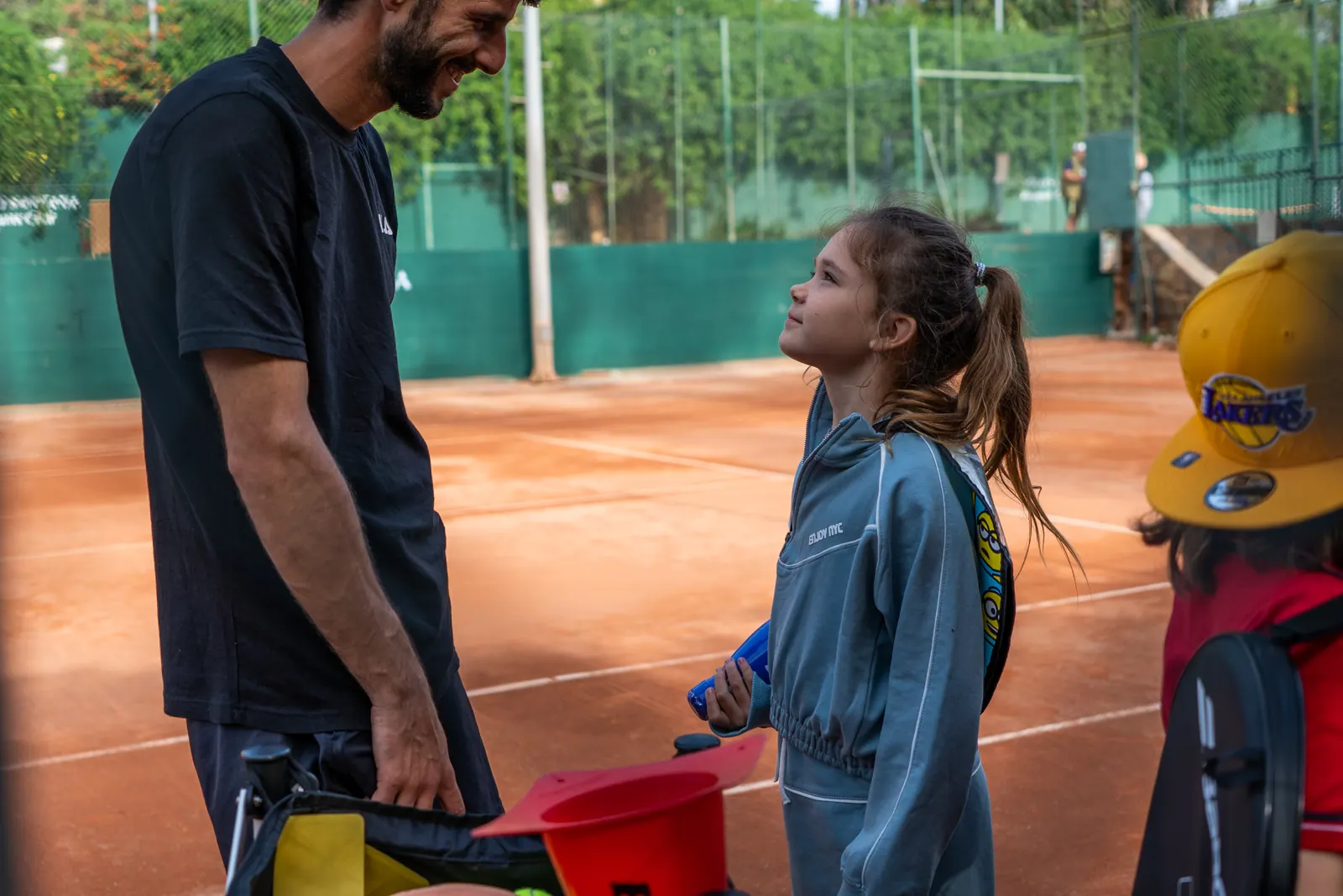 Profesor hablando con una alumna de la escuela infantil en pista de tierra batida